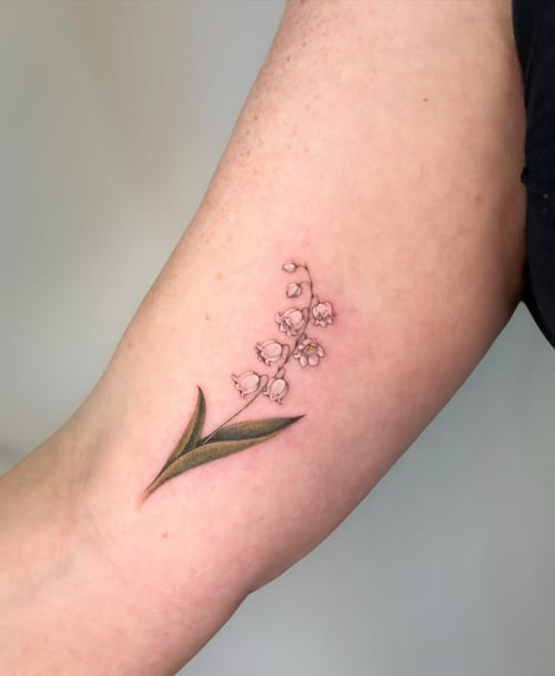 A delicate fine line tattoo of a lily of the valley on the inner arm with subtle color accents — by Melanie Benoit, los angeles