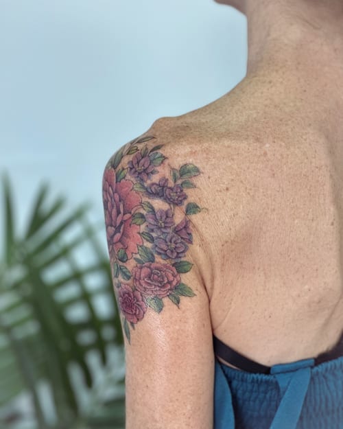 A colorful floral bouquet tattoo on the shoulder featuring roses and other flowers in a delicate and romantic style — by Melanie Benoit, los angeles