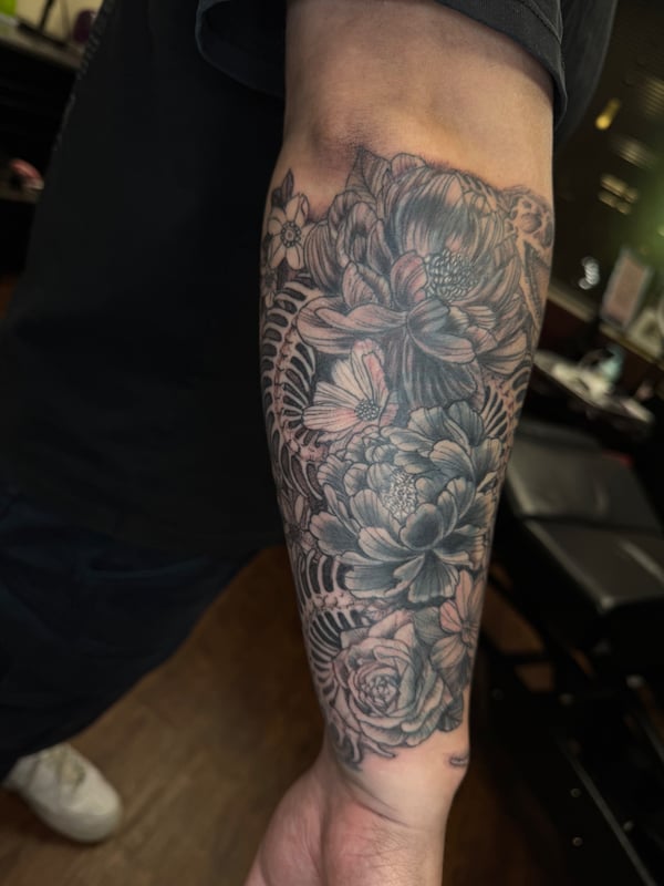 A delicate black and grey floral arrangement tattoo on the forearm, featuring detailed flowers and intricate shading — by Sandra Price, ventura, ca