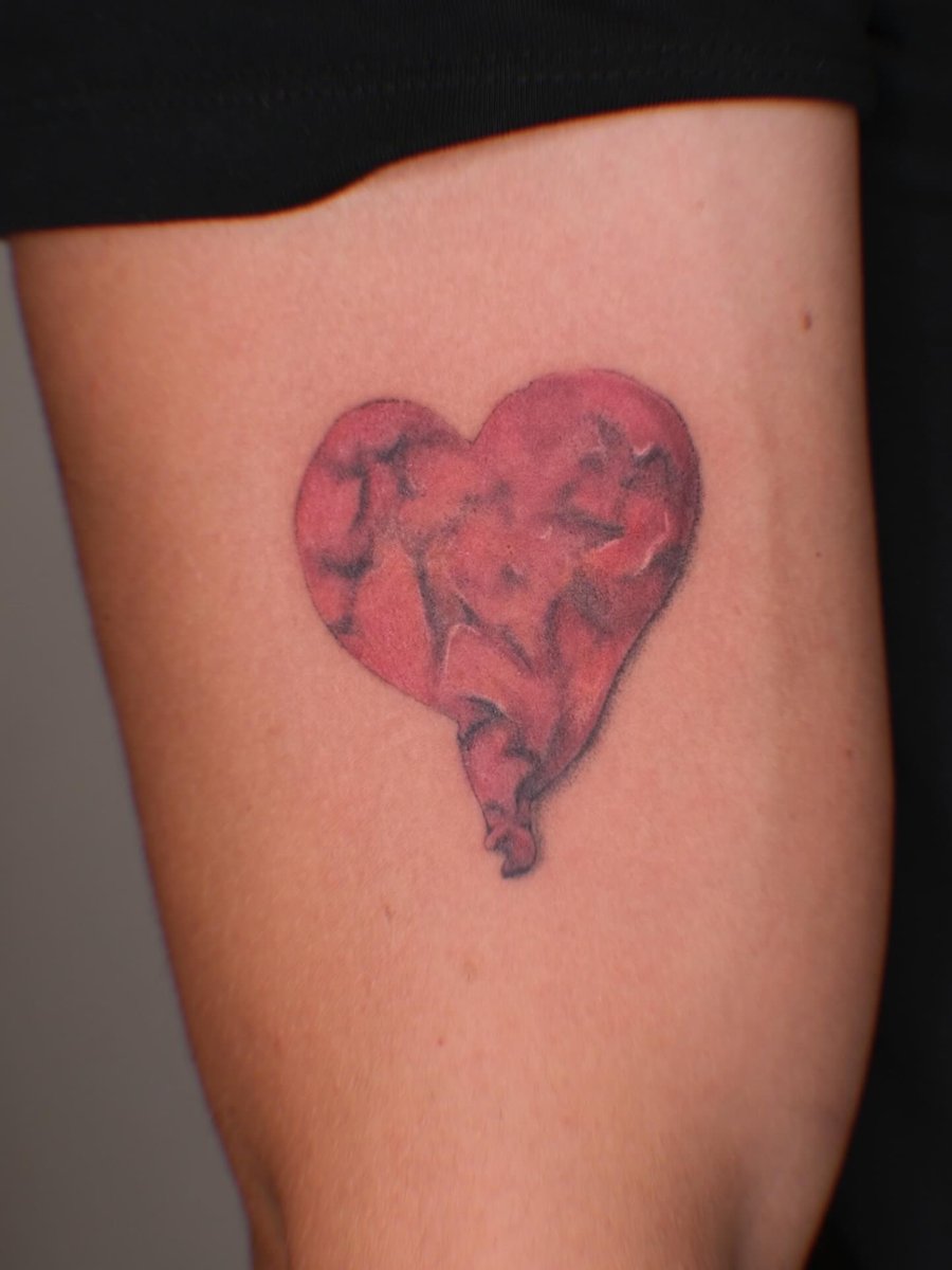 A red abstract heart tattoo on the upper arm with an illustrative style — by Samantha Wilks, los angeles