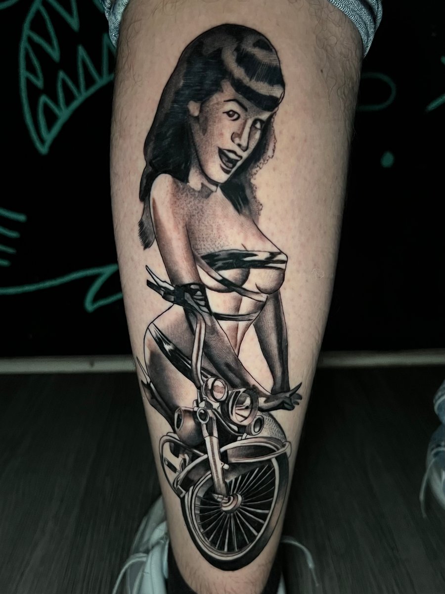 A black and grey realistic tattoo on the calf depicting a woman sitting on a motorcycle, with detailed shading and a vintage style — by Josue Bravo, los angeles
