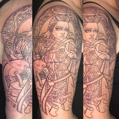 A bold black and grey linework tattoo of a warrior woman with a sword and Celtic designs on the upper arm — by Sandra Price, los angeles