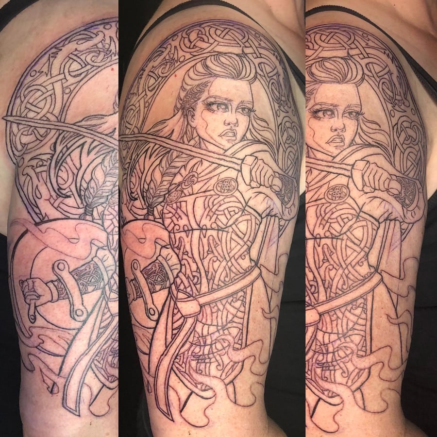 A bold black and grey linework tattoo of a warrior woman with a sword and Celtic designs on the upper arm — by Sandra Price, los angeles