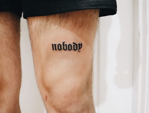 A minimal black script lettering tattoo on the thigh reading 'nobody' — by Level tattoo, los angeles