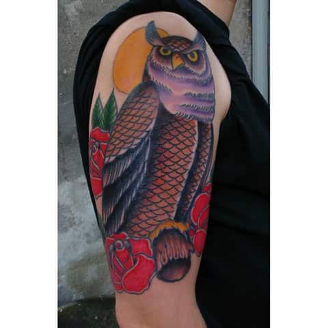 A bold American traditional style tattoo of an owl with roses on the upper arm, featuring vibrant colors and classic design elements — by Samuel Connelly, los angeles