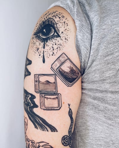 A surreal black and grey tattoo on the upper arm featuring an eye with tears and multiple televisions displaying waves — by Level tattoo, los angeles