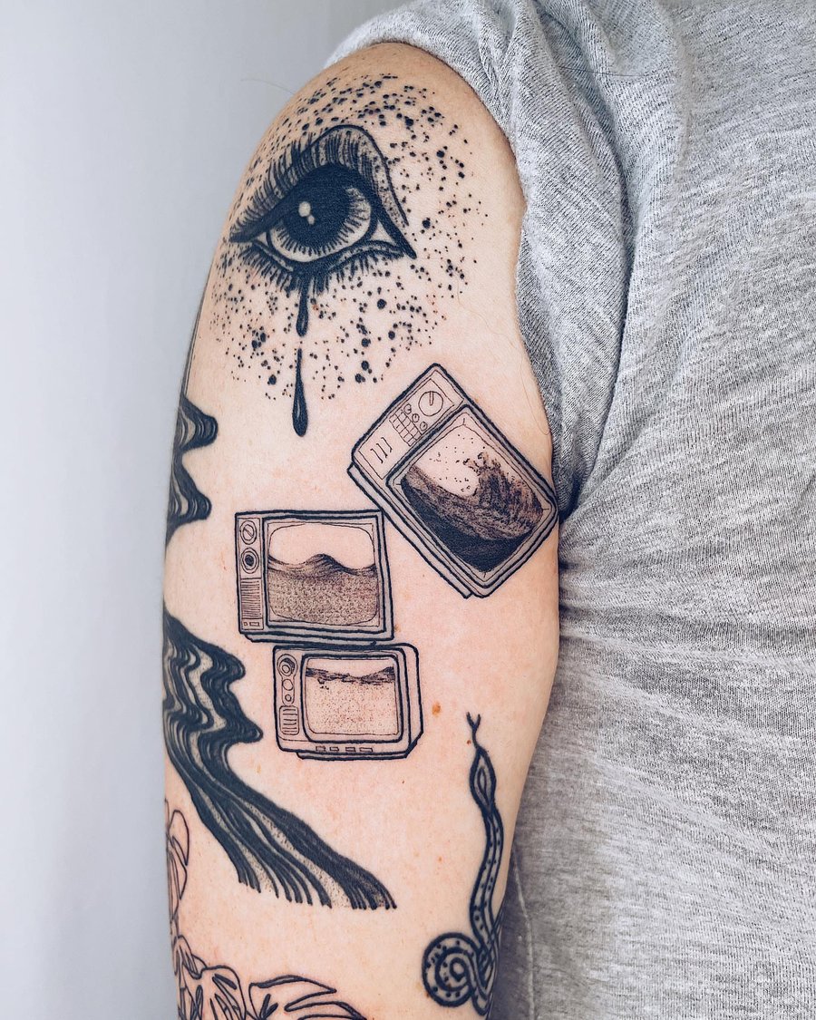 A surreal black and grey tattoo on the upper arm featuring an eye with tears and multiple televisions displaying waves — by Level tattoo, los angeles