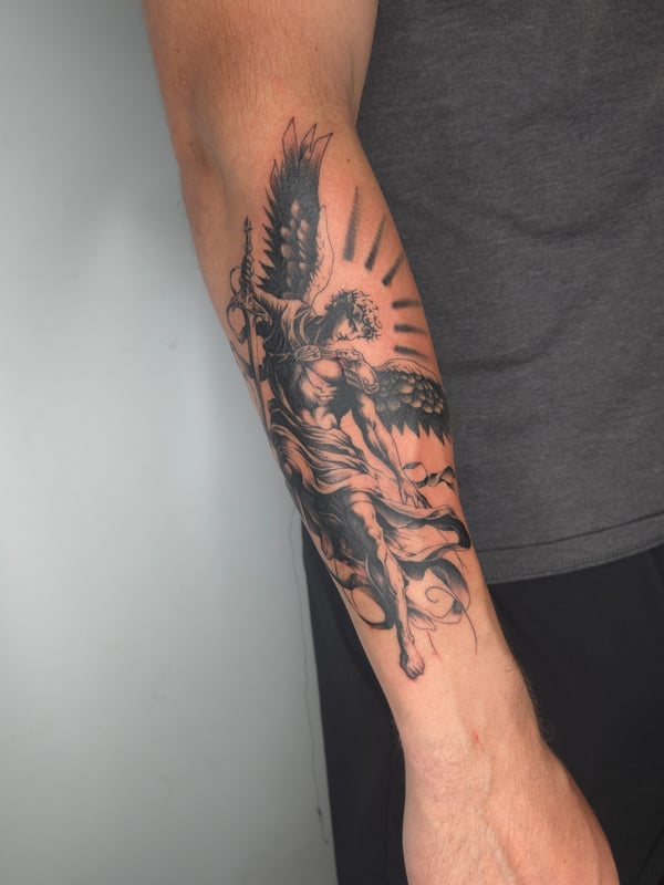 A detailed black and grey tattoo of an angel with wings on the forearm, featuring realistic shading and dynamic movement — by ashynucklestattoo, los angeles