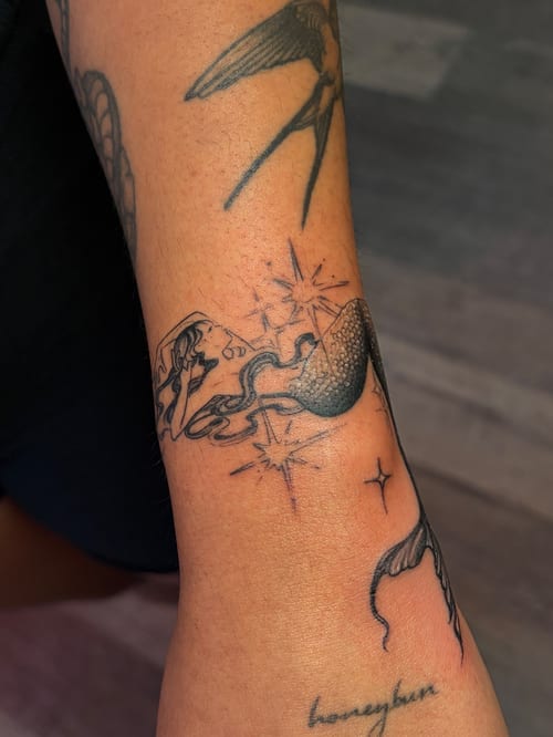 A fine line blackwork tattoo of a mermaid with stars on the forearm, featuring delicate linework and shading — by Vince Espinoza, los angeles