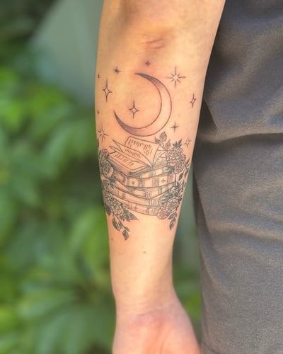 A delicate black and grey tattoo of a stack of books with a crescent moon and stars on the forearm, featuring fine line floral details — by Sandra Price, los angeles