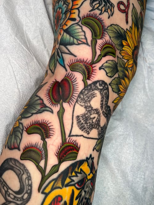 A colorful Neo-Traditional tattoo on the arm featuring vibrant flowers and botanical elements with bold outlines and shading — by Megan Rose, los angeles