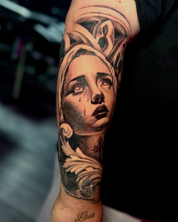 A realistic black and grey portrait of a woman's face with tears on the arm, featuring detailed shading and ornate elements — by zealous, los angeles