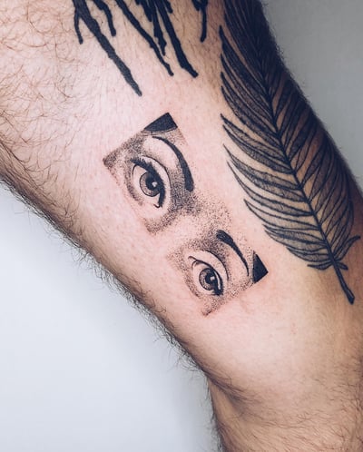 A bold black and grey dotwork tattoo of eyes on the leg, featuring graphic elements and strong contrast — by Level tattoo, los angeles