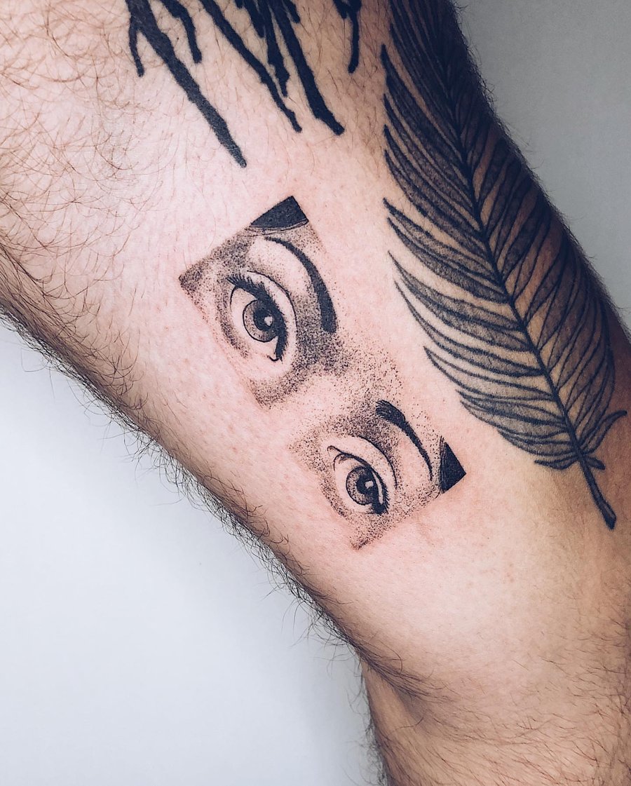 A bold black and grey dotwork tattoo of eyes on the leg, featuring graphic elements and strong contrast — by Level tattoo, los angeles