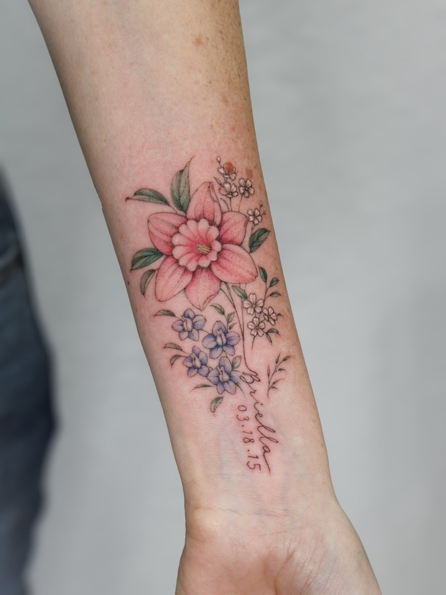 A delicate color floral tattoo on the forearm featuring a mix of flowers with fine line details and script lettering — by Melanie Benoit, los angeles