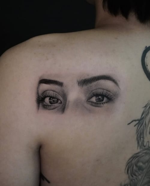 A black and grey realism tattoo of a pair of eyes on the back, showcasing detailed shading and lifelike features — by Jian Liang, los angeles