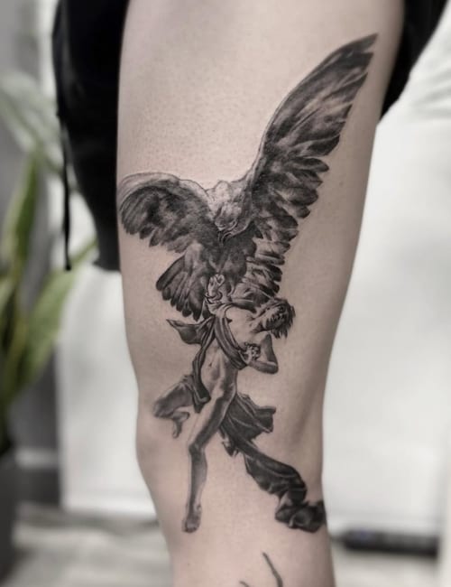 A black and grey realism tattoo of an angel with wings spread wide, located on the thigh with detailed shading — by Jian Liang, los angeles