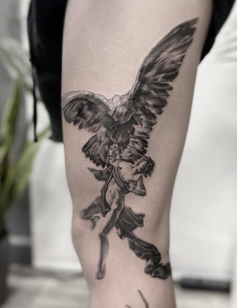 A black and grey realism tattoo of an angel with wings spread wide, located on the thigh with detailed shading — by Jian Liang, los angeles