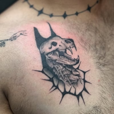 A graphic black and grey skull with fangs and chains tattoo on the chest — by Maddie Ramirez, los angeles