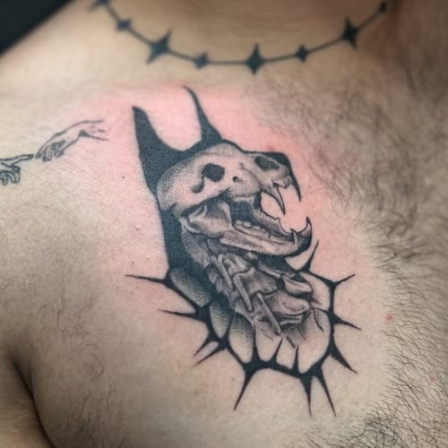 A graphic black and grey skull with fangs and chains tattoo on the chest — by Maddie Ramirez, los angeles