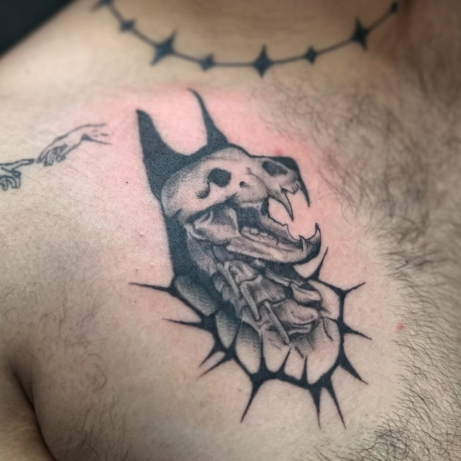 A graphic black and grey skull with fangs and chains tattoo on the chest — by Maddie Ramirez, los angeles