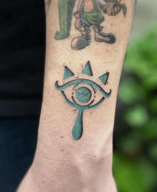 A colorful illustrative tattoo of an eye with geometric elements on the forearm, featuring bold outlines and vibrant colors — by Jian Liang, los angeles