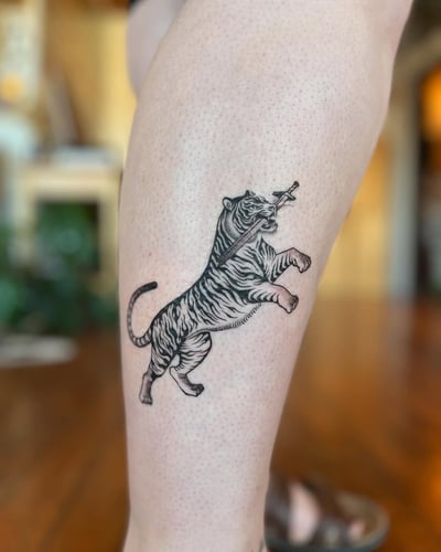 A bold blackwork tattoo of a tiger holding a sword on the calf, featuring strong lines and graphic style — by Dylan Aiello, los angeles
