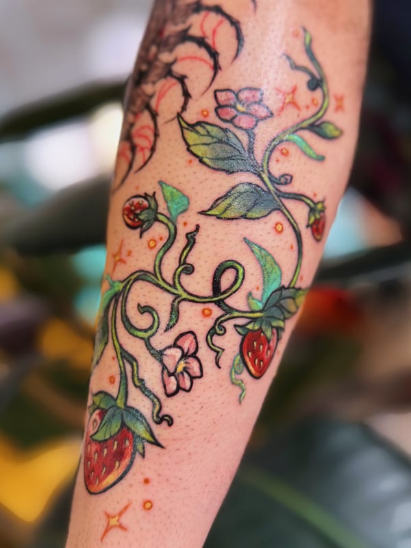 A colorful neo-traditional tattoo on the forearm featuring strawberries and flowers with vibrant green leaves and red berries — by Tweetwee, west covina, ca