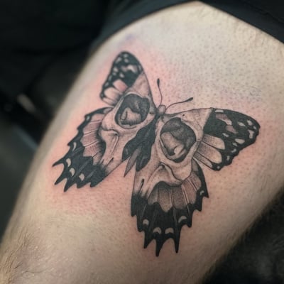 A black and grey butterfly tattoo with skulls on the wings, located on the thigh — by Maddie Ramirez, los angeles