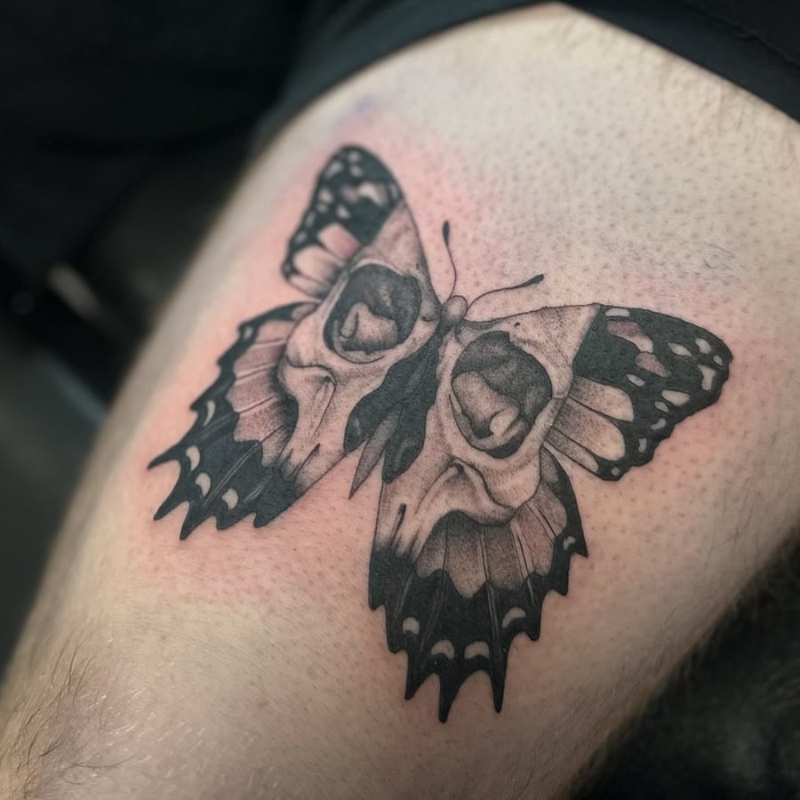 A black and grey butterfly tattoo with skulls on the wings, located on the thigh — by Maddie Ramirez, los angeles