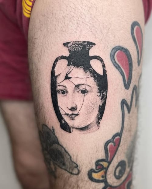 A black and grey portrait of a woman's face within a vase shape on the thigh, featuring bold lines and shading — by Level tattoo, los angeles