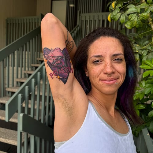 A bold and colorful neo-traditional tattoo of a cartoon character with 'poison' text on the inner arm — by Sandra Price, los angeles