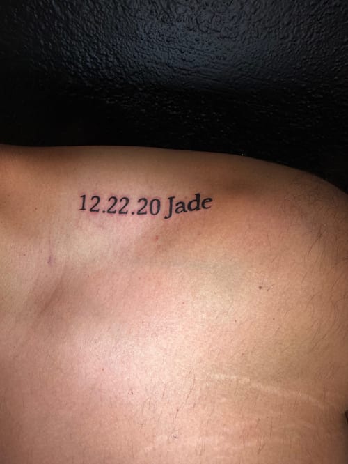 A minimalist black and grey tattoo of a date and name on the shoulder, featuring simple script lettering — by Kiera Garvin, los angeles