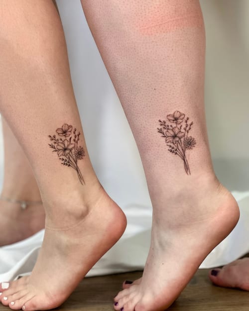 A delicate fine line flower bouquet tattoo on the ankle in black and grey, featuring minimalistic floral elements — by Melanie Benoit, los angeles