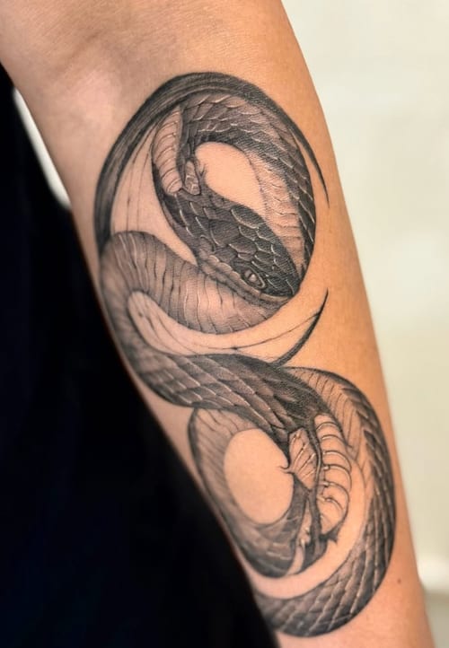 A black and grey tattoo of a coiled snake on the forearm, featuring detailed linework and shading — by otaybeatdown, los angeles