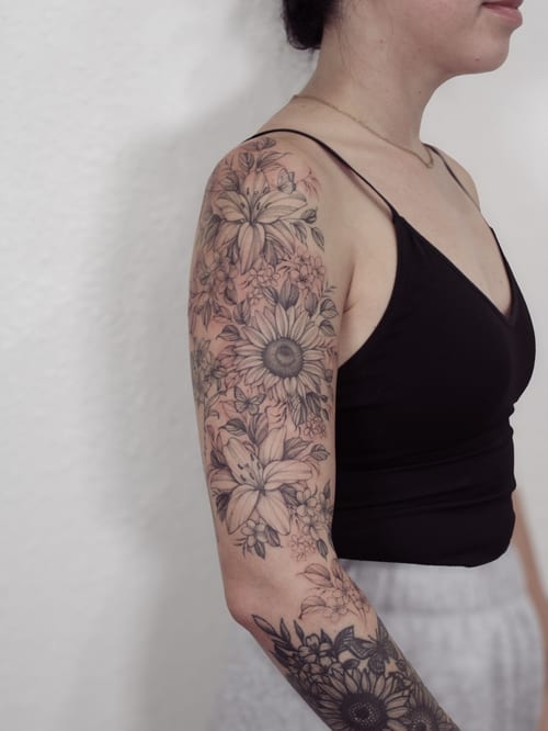 A delicate black and grey floral bouquet tattoo on the arm, featuring detailed flowers and leaves — by Melanie Benoit, los angeles