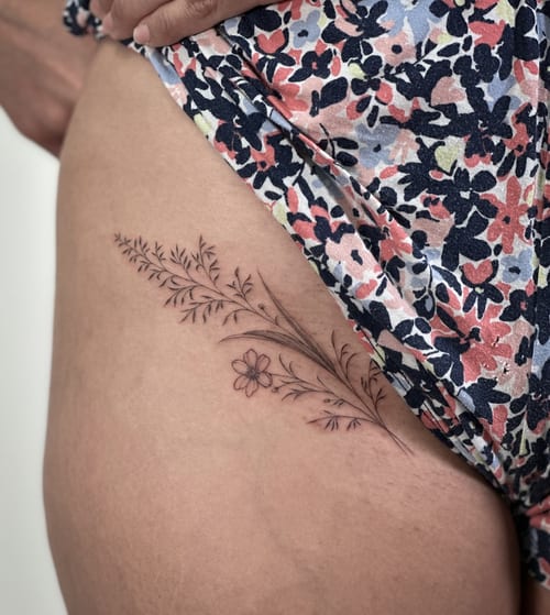 A delicate black and grey floral branch tattoo on the hip, featuring fine line work and minimalist style — by Melanie Benoit, los angeles