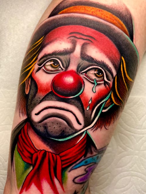 A colorful Neo-Traditional tattoo of a sad clown face on the leg, featuring bold outlines and vibrant shading — by Megan Rose, los angeles