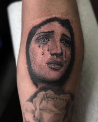 A black and grey portrait of a woman's face with tears on the arm, featuring delicate shading and blackwork style — by Maddie Ramirez, los angeles