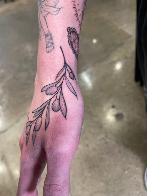 A fine line black and grey tattoo of a simple floral branch on the hand, featuring delicate leaves and minimalistic design — by Vince Espinoza, los angeles