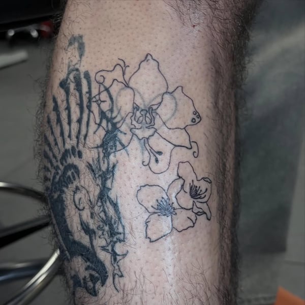 A black and grey tattoo on the leg featuring flowers and a skull in a graphic linework style — by Hannah , fountain valley, ca