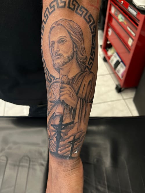 A black and grey realism portrait of Jesus Christ on the forearm, featuring detailed shading and a religious theme — by Mr._Folks, los angeles