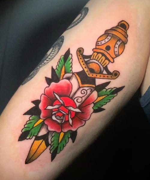 A colorful American Traditional style tattoo of a dagger piercing a rose on the arm, featuring bold outlines and vibrant colors — by Shelby Bianco, los angeles