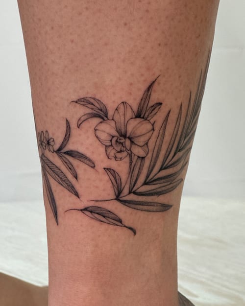 A delicate black and grey fine line tattoo of flowers and leaves on the leg, showcasing a minimalist botanical design — by Melanie Benoit, los angeles