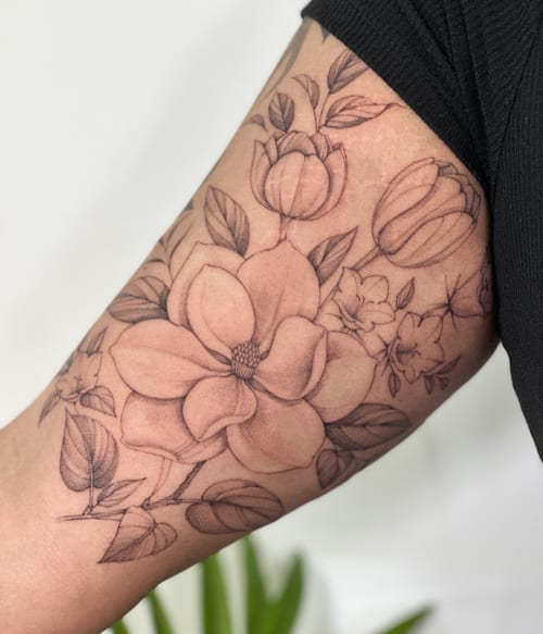 A delicate black and grey flower bouquet tattoo on the upper arm, featuring detailed floral designs — by Melanie Benoit, los angeles