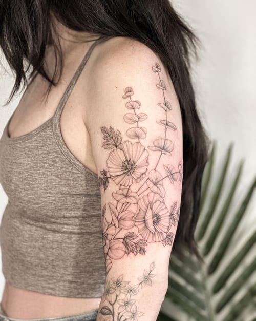 A delicate black and grey floral arrangement on the upper arm, featuring fine line work and minimalistic design — by Melanie Benoit, los angeles