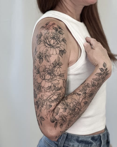 A delicate black and grey floral sleeve tattoo covering the full arm with intricate flower designs — by Melanie Benoit, los angeles