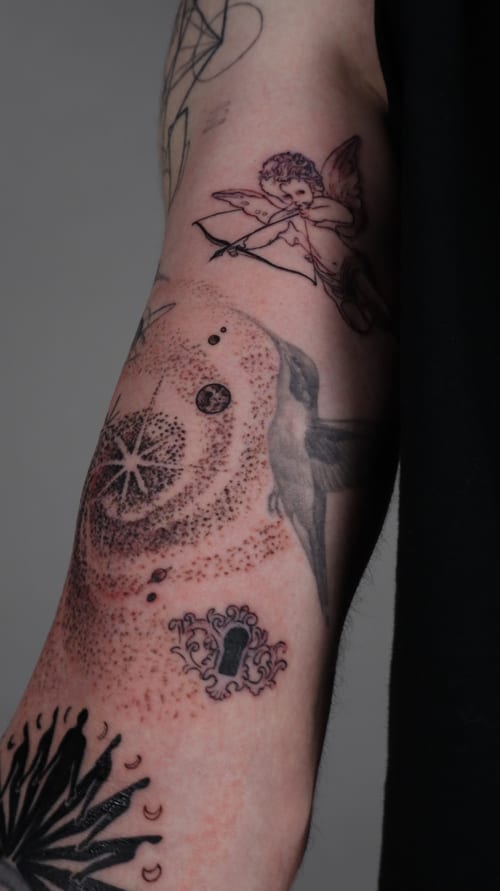 A black and grey tattoo on the forearm featuring an angel with a bow and arrow, a bird, and dotwork patterns, showcasing intricate blackwork and dot shading — by Vince Espinoza, los angeles