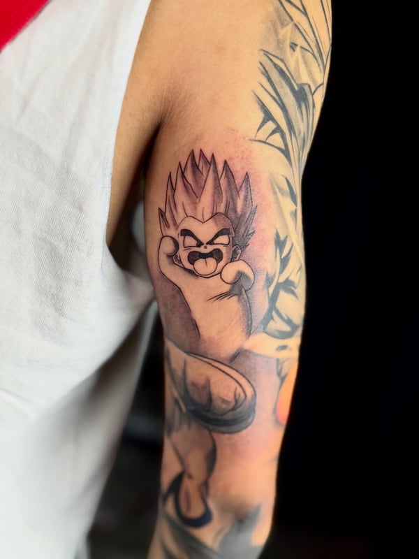 A bold black and grey anime character tattoo on the upper arm, featuring dynamic lines and shading — by zealous, los angeles