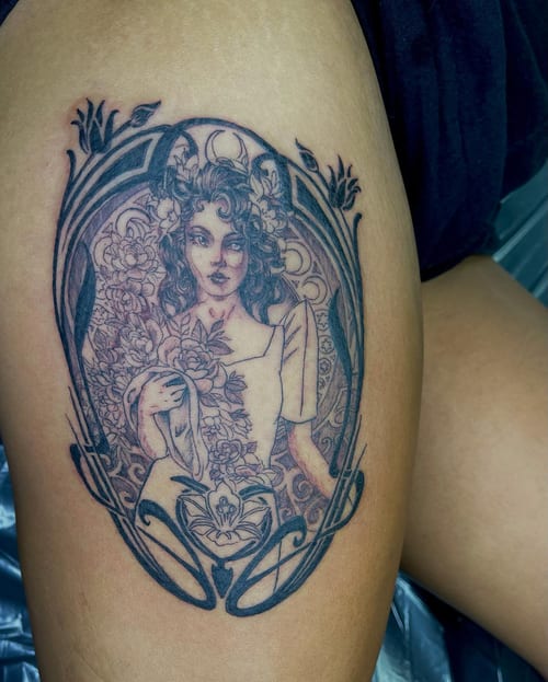 An ornate black and grey tattoo of a woman with floral elements on the thigh, featuring detailed linework and shading — by Sandra Price, los angeles